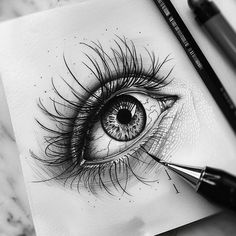 a pencil drawing of an eye with long lashes on paper next to a pen and marker