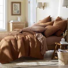 a bed with brown sheets and pillows in a bedroom next to a lamp on a dresser