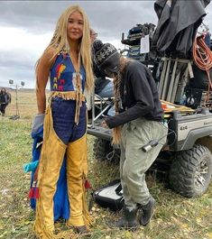 a man and woman standing next to a truck with an atv in the back ground