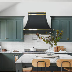 a kitchen with green cabinets and a black range hood over the island in front of it