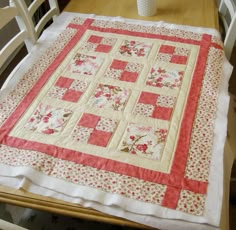 a quilted table runner on top of a wooden dining room table with white chairs