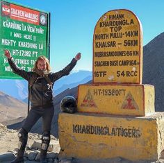 a woman standing in front of a sign on top of a mountain with her arms up