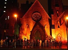 an old church lit up at night with people standing in the front and on the side