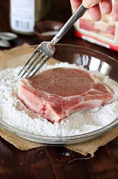 a person is using a fork to cut up meat on top of flour in a glass bowl