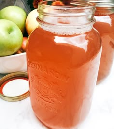 three jars filled with liquid sitting next to apples