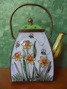 a teapot with flowers painted on it sitting on a table next to a green wall