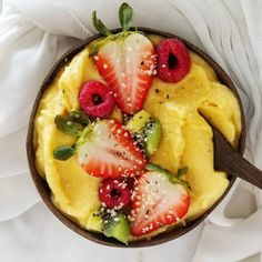 a bowl filled with fruit on top of a white cloth next to a wooden spoon