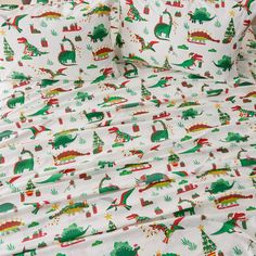 a white bed with dinosaurs and trees printed on the sheet set, along with matching pillow cases