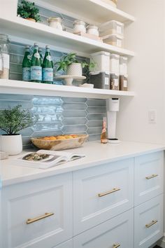 a kitchen with white cabinets and shelves filled with bottles, dishes, and other items