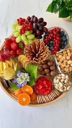 a platter filled with fruit and nuts on top of a white table next to a potted plant