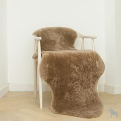 a chair made out of sheepskin with a wooden armrest and back rests against a white wall