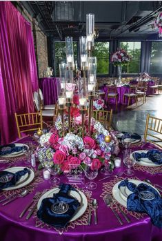 the table is set with purple linens, silverware and pink flowers in vases