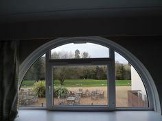 an open window with chairs and tables in front of the grass field through which there are trees