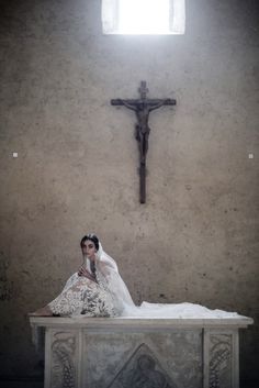 a woman sitting on top of a white table in front of a cross