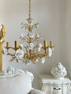 a chandelier hanging from the ceiling next to a white chair and table with flowers on it