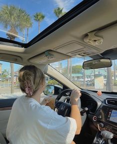 a woman driving a car with palm trees in the background