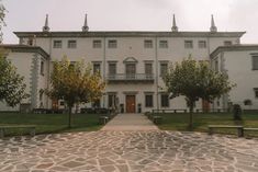 a large white building with benches in front of it and trees on the other side