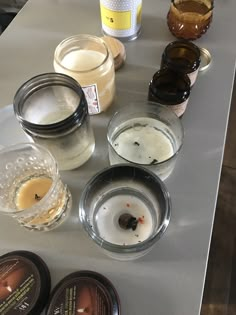 several different types of candles sitting on a table top next to jars and containers filled with liquid