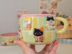 a hand holding a coffee mug with cats on it and other items around the cup