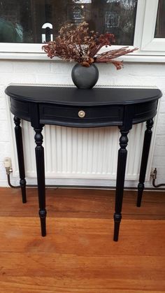 a black table sitting in front of a window with a vase on top of it