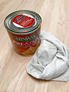 a can of wax next to a cloth on a wooden table with a white towel