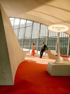 a man and woman are walking through an airport lobby with red carpet on the floor