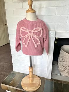 a pink sweater with a bow is on a mannequin next to a fireplace