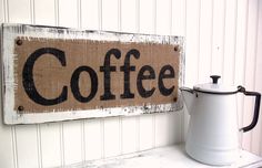 a white coffee pot sitting on top of a wooden shelf next to a sign that says coffee