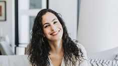 a woman sitting on top of a white couch next to a window and smiling at the camera