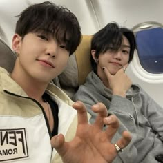 two young men sitting on an airplane with their hands in the air