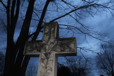 a large cross sitting in the middle of a forest next to a tree with no leaves on it