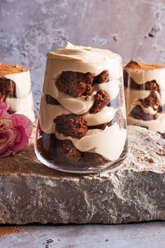 three desserts in glass containers sitting on top of a stone slab with pink flowers