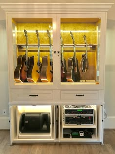 an entertainment center with guitars and amps in the glass doored display case on top