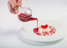 someone pouring sauce onto a dessert on a white plate with red crumbled toppings