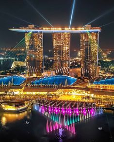 an aerial view of the marina bay area at night, with lights and water fountains in the foreground