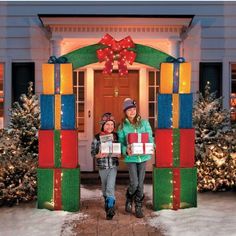 two girls are standing in front of a house decorated with christmas lights and presents for the holiday season