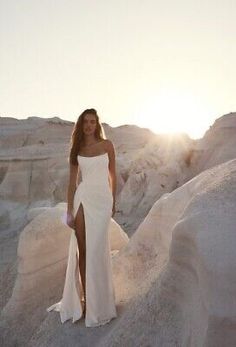 a woman in a white dress standing on some rocks