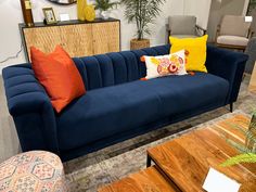 a blue couch with orange and yellow pillows on it in a room filled with furniture