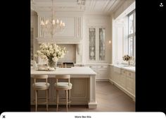 a white kitchen with chandelier, counter and stools next to the sink