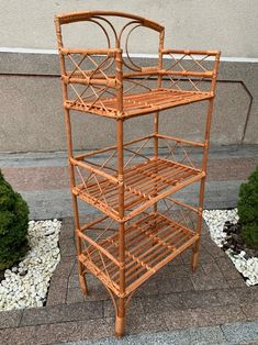 a bamboo shelf sitting on top of a sidewalk next to some rocks and plants in front of a building