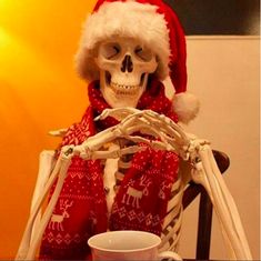 a skeleton dressed up as santa clause sitting at a table with a cup and saucer