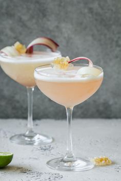 two glasses filled with drinks and garnished with fruit