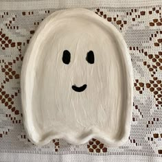 a white plate with a face painted on it sitting on a lace tablecloth covered surface