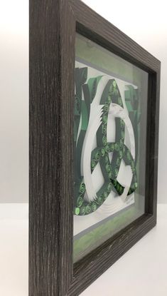 an art piece in a wooden frame with green and white designs on the front side