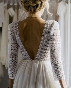 a woman standing in front of a rack of wedding gowns and looking down at her dress