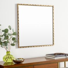 a mirror on the wall above a dresser with a vase and plant next to it