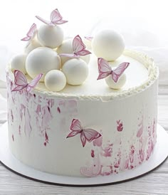 a white cake with pink butterflies and eggs on top, sitting on a wooden table