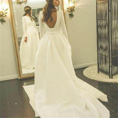 a woman standing in front of a mirror wearing a white wedding dress with long sleeves