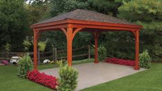 a wooden gazebo sitting in the middle of a lush green yard with red flowers