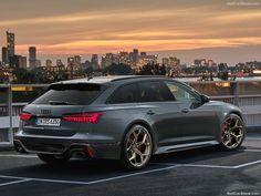 the rear end of a grey car parked in a parking lot with city lights behind it